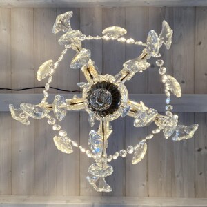 May include: A crystal chandelier with a gold finish and multiple tiers of crystal drops. The chandelier is hanging from a wooden ceiling.