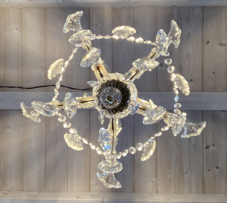 May include: A crystal chandelier with a gold finish and multiple tiers of crystal drops. The chandelier is hanging from a wooden ceiling.