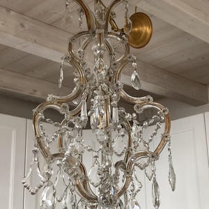 May include: A large, ornate crystal chandelier with a gold finish. The chandelier has multiple tiers of crystal drops and is hanging from a white ceiling.