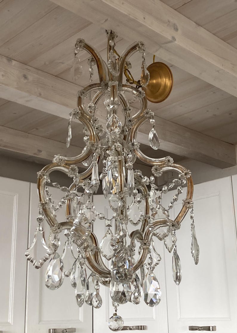 May include: A large, ornate crystal chandelier with a gold finish. The chandelier has multiple tiers of crystal drops and is hanging from a white ceiling.