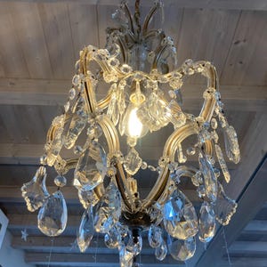 May include: A crystal chandelier with a gold frame and many hanging crystal drops. The chandelier is hanging from a wooden ceiling.