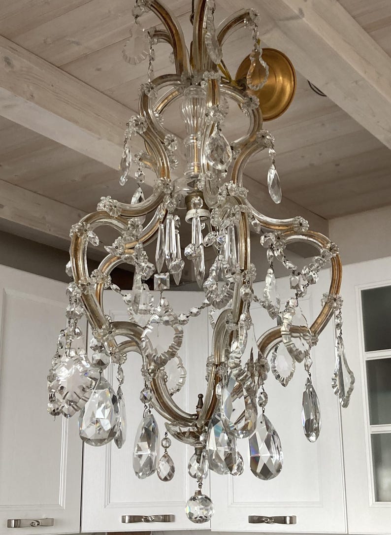 May include: A large, ornate crystal chandelier with a gold finish. The chandelier has multiple tiers of crystal drops and is hanging from a white ceiling.