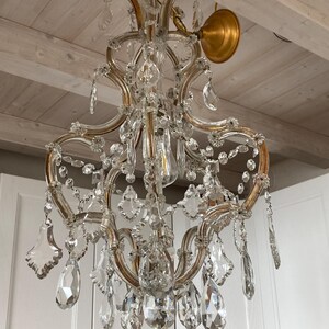 May include: A crystal chandelier with a gold finish and a delicate, ornate design. The chandelier features multiple tiers of crystal drops and is suspended from a gold chain.