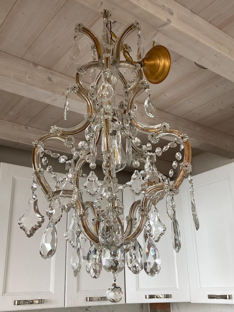 May include: A crystal chandelier with a gold finish and a delicate, ornate design. The chandelier features multiple tiers of crystal drops and is suspended from a gold chain.