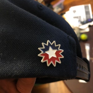 May include: A black baseball cap with a silver star-shaped pin. The pin has red and white stripes and a white star in the center.