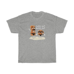 Op de afbeelding: Een grijs T-shirt met een afbeelding van twee cartoon-broodjes die een zonnebril dragen. De tekst "Suns Out Buns Out" is op het shirt gedrukt.