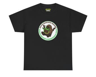 Op de afbeelding: Zwart T-shirt met een cirkelvormige afbeelding van een stripfiguur die een boek leest. De afbeelding bevat de tekst "READ BANNED BOOKS GAIN FORBIDDEN KNOWLEDGE" in een groene cirkel. Het shirt heeft ook de tekst "BEYOND PERIL" bovenaan.