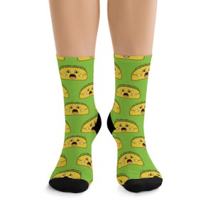 May include: A pair of green socks with a repeating pattern of yellow cartoon tacos with a surprised expression. The socks are black at the toes and heels.