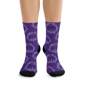 May include: Purple socks with a repeating pattern of a black creature with red eyes. The creature is stylized to look like a monster.