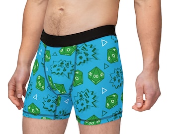 Op de afbeelding: Blauwe boxershorts met een zwarte tailleband en een herhalend patroon van groene dobbelstenen, uitroeptekens en schedelafbeeldingen. De shorts hebben een comfortabele pasvorm en zijn gemaakt van zacht materiaal.