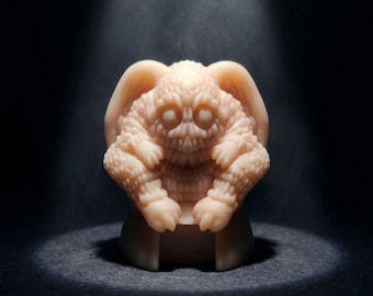 Op de afbeelding: Een lichtbeige, getextureerd beeldje van een wezen met grote oren, een skeletachtig gezicht en klauwachtige handen en voeten. De figuur wordt verlicht door een schijnwerper tegen een donkere achtergrond.