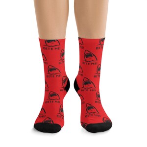 Könnte beinhalten: Rote Socken mit einem schwarzen Hai-Motiv und dem Text "BITE ME!" wiederholt über das gesamte Design.