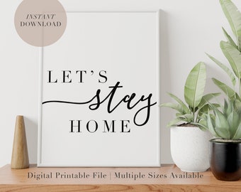 Może przedstawiać: Biały, drukowany plakat z czarnym tekstem, który brzmi "Let's stay home". Plakat jest oprawiony i stoi na drewnianym stole z dwoma roślinami w doniczkach.
