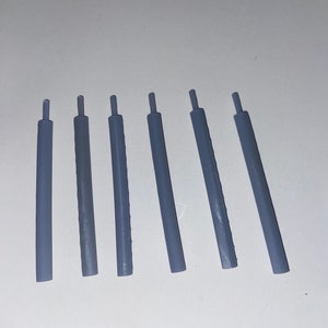 May include: Six gray plastic rods, all the same size and shape, are arranged in a row on a white surface.