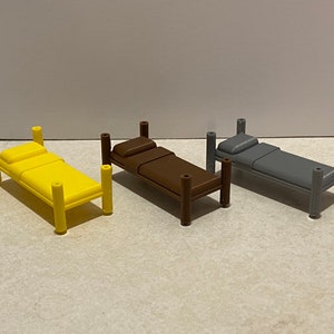 May include: Three miniature beds in yellow, brown, and gray. Each bed has a rectangular mattress and a pillow. The beds have four cylindrical posts at each corner. The beds are designed for a dollhouse or miniature setting.