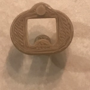 May include: A 3D printed beige bottle opener with a rounded shape and a square opening for the bottle cap.