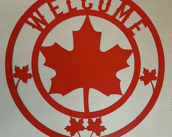 Könnte beinhalten: Rotes Metall-Willkommensschild mit Ahornblatt-Design. Das Wort "WELCOME" ist am Rand des Kreises ausgeschnitten, mit einem großen Ahornblatt in der Mitte. Kleine Ahornblätter sind um den Kreis herum platziert.