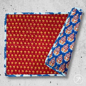May include: A rectangular quilted fabric mat featuring a deep red base with a repeating pattern of small yellow flowers. The mat has a blue border with a white floral print, and one corner is folded back to reveal a blue underside with large floral motifs.