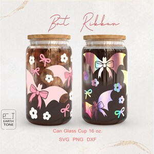 Puede incluir: Dos vasos de vidrio transparente con tapas de madera, decorados con diseños de murciélagos y lazos. Una taza presenta un murciélago y un lazo rosa, la otra un murciélago y un lazo holográficos. Los vasos son de 473 ml.