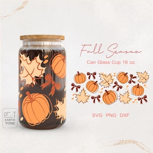 Puede incluir: Un vaso de vidrio transparente con forma de lata y tapa de madera, decorado con calabazas naranjas, hojas de otoño y lazos. La taza está etiquetada como "Fall Season" y "Can Glass Cup 16 oz."