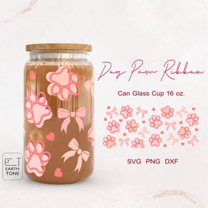 Op de afbeelding: Een glazen blikbeker van 473 ml met een roze pootprint- en strikdesign. De tekst "Dog Paw Ribbon" is in cursief boven de beker geschreven. De tekst "Can Glass Cup 16 oz." is onder de beker geschreven. De tekst "SVG PNG DXF" is onder de beker geschreven.