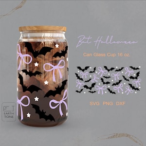Op de afbeelding: Een glazen beker in de vorm van een blikje met een houten deksel, versierd met zwarte vleermuissilhouetten, lavendelkleurige strikken en witte sterren. De tekst "Bat Halloween" en "Can Glass Cup 16 oz." zijn zichtbaar. De beker is gevuld met een bruine vloeistof.