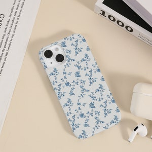 May include: A white phone case with a blue floral pattern. The case has a camera cutout and a white background.