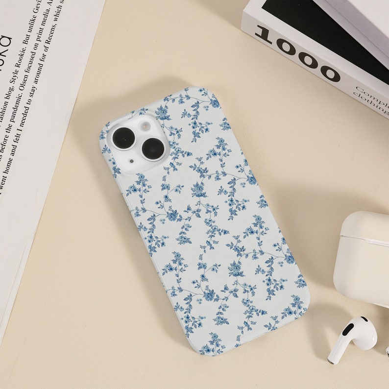 May include: A white phone case with a blue floral pattern. The case has a camera cutout and a white background.