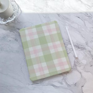 May include: A green and pink plaid iPad case with a white stylus on a marble surface.