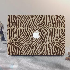 Könnte beinhalten: Eine Laptop-Hülle mit einem Zebra-Print-Design in Braun- und Beigetönen. Das Apple-Logo ist in der Mitte sichtbar. Die Hülle ist für Laptops konzipiert und bietet einen stilvollen, tierisch inspirierten Look. Maße: ca. 33 cm x 23 cm.