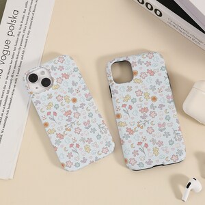 May include: Two phone cases with a light blue background and a pattern of small white flowers, pink flowers, yellow flowers, and small cartoon bears.