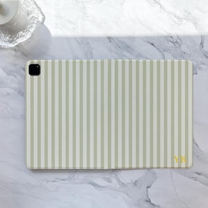 May include: A light green and white striped tablet case with a camera cutout. The case has the initials "YK" in gold on the bottom right corner. The case is rectangular and has a smooth surface.