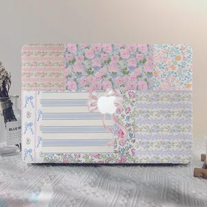 Puede incluir: Una piel para portátil con un diseño de patchwork con motivos florales en tonos rosa, azul y blanco. La piel tiene un logotipo de Apple blanco en el centro.