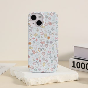 May include: A white phone case with a cute floral pattern featuring small animals, hearts, and moons. The case has a camera cutout and a light blue background.
