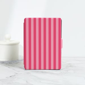 May include: A pink and light pink striped tablet case. The case has a vertical stripe pattern and a pink clasp on the side. The case is rectangular and appears to be made of a smooth material.