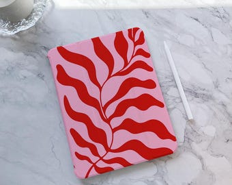 May include: A pink tablet case with a red, stylized botanical design. A white stylus lies beside the case. The case features a repeating pattern of curved, leaf-like shapes. The overall aesthetic is modern and artistic.