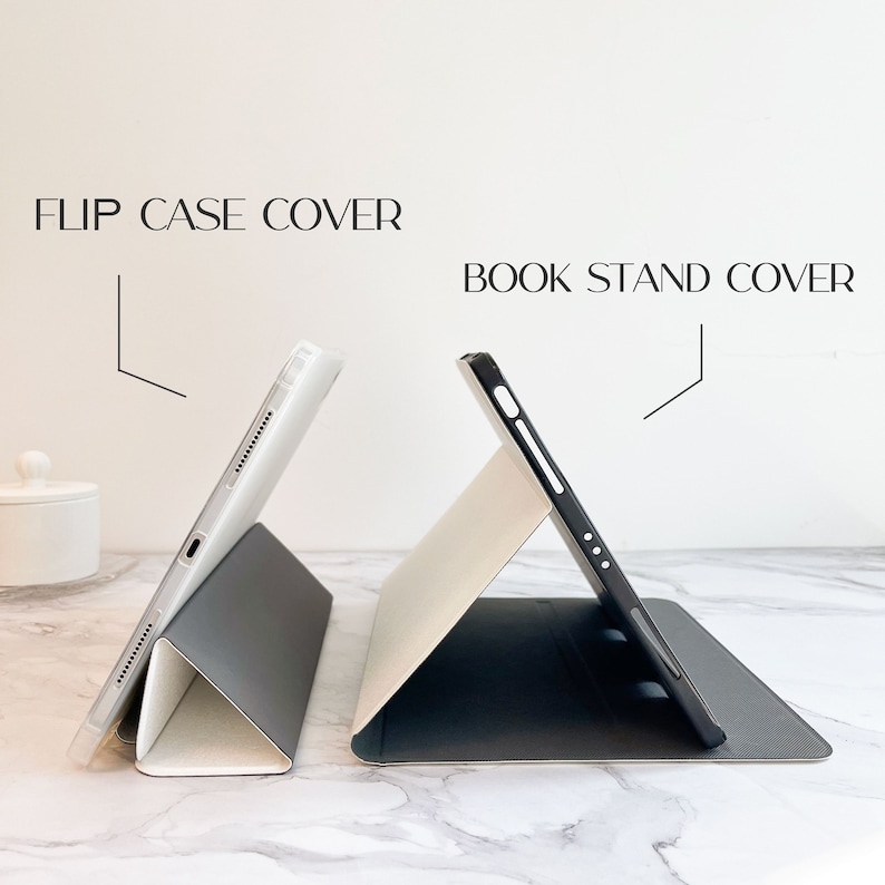 May include: Two tablet cases are shown, one labelled "FLIP CASE COVER" and the other "BOOK STAND COVER." The cases are in a stand position, demonstrating their design. The cases have a neutral colour scheme, with a mix of grey, white, and black.