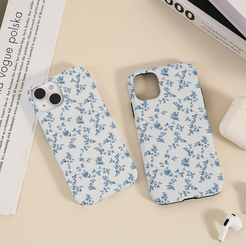 May include: Two white phone cases with a blue floral pattern. The cases have a black border and a cutout for the camera lens.