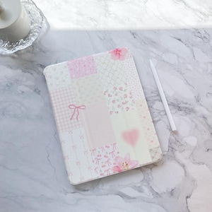 Könnte beinhalten: Eine iPad-Hülle mit einem rosafarbenen und weißen Patchwork-Design, einem Blumenmuster und rosa Schleifen.