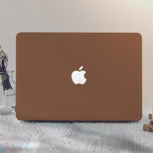 以下が含まれることがあります： 白いテーブルクロスの上に置かれた、蓋に白いアップルのロゴが付いた茶色のラップトップコンピューターです。