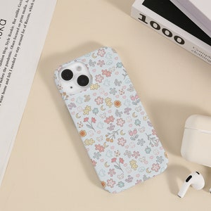 May include: A light blue phone case with a white background and a repeating pattern of small flowers, hearts, moons, and bears.