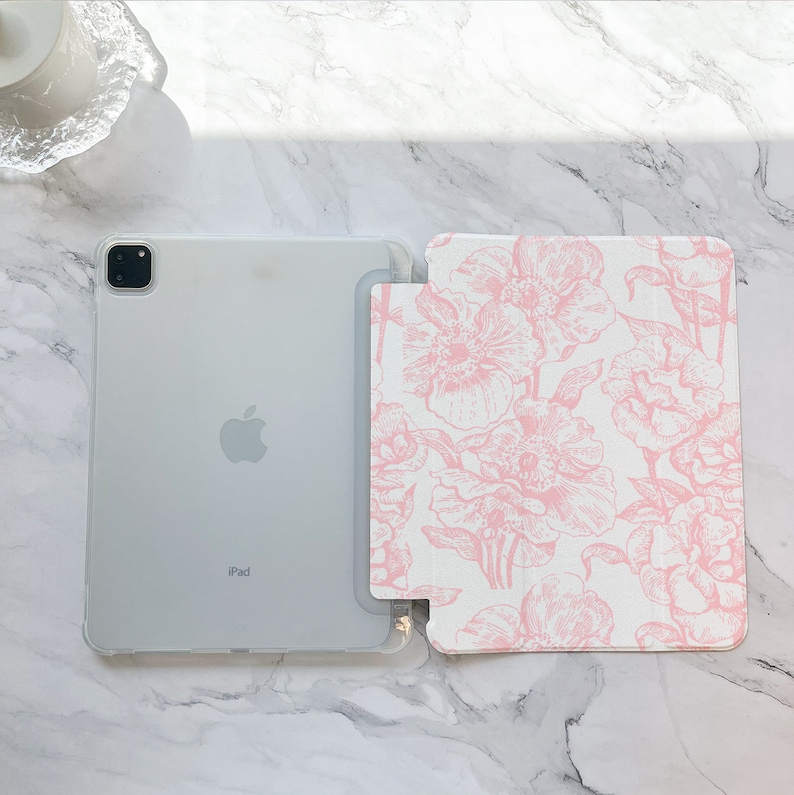 May include: A white iPad case with a pink floral design. The case has a clear back and a floral front. The iPad is visible through the clear back.