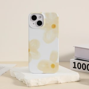 May include: White iPhone case with a floral design featuring yellow flowers. The case has a cutout for the camera lens.