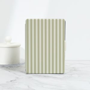 May include: A light green and white striped tablet case with a magnetic closure. The case is rectangular and has a vertical stripe pattern. A white ceramic jar with a lid is in the background.