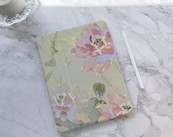 May include: A floral-patterned tablet case featuring large pink and purple flowers on a light green background. A white stylus rests beside the case on a marble surface. The case has a soft, watercolor-like design.