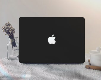 Könnte beinhalten: Ein schwarzer Laptop mit einem weißen Apple-Logo auf dem Deckel. Der Laptop steht auf einer weißen Tischdecke.