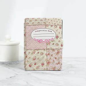 Puede incluir: Una cubierta de cuaderno con estampado floral rosa y blanco con una etiqueta ovalada blanca que dice "composition book".