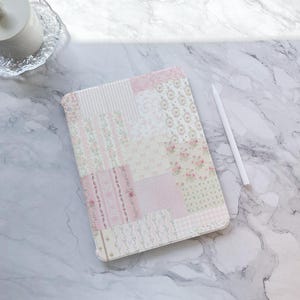 Può includere: Una custodia per iPad con un design a patchwork rosa e bianco con un motivo floreale.