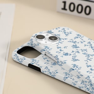May include: White phone case with a blue floral pattern. The case has a cutout for the camera lens.