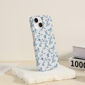May include: A white phone case with a blue floral pattern. The case has a camera cutout and is designed for an iPhone.